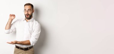 Büyük nesneler gösteren hayret verici iş adamı, beyaz arka planda duran, büyük ve heyecanlı görünen bir şey tarif et..