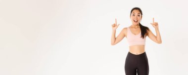 Spor, refah ve aktif yaşam tarzı konsepti. Heyecanlı ve mutlu Asyalı spor giyim kızı, parmaklarını havaya kaldırıyor ve büyük indirimlerle şaşkın bakıyor, afiş okuyor, beyaz arka plan.