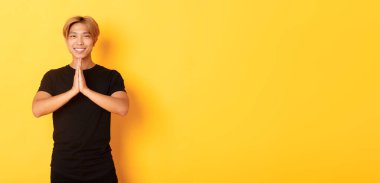 Minnettar gülümseyen Asyalı sarışının portresi dua ederek el ele tutuşuyor, sarı arka planda duruyor..