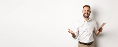 Tatmin olmuş işadamı iyi işi överek, dijital tablet hakkında rapor okuyarak, beyaz arka plana karşı mutlu bir şekilde duruyor..