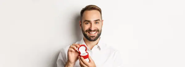 近くに幸せなハンサムな男の提案を ボックス内の結婚指輪を保持し 笑みを浮かべて 彼と結婚するように求めて 白の背景 — ストック写真