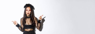 Gotik makyaj ve çelenk ile küstah genç kötü cadı, yan tarafı göstererek kibirli görünüyor, iki cadılar bayramı temalı bayrak gösteren, beyaz arka plan üzerinde duran.