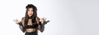 Cadı gibi giyinmiş cadılar bayrağının sol üst köşesine bakıp gülümseyen cadılar bayrağını ya da logonuzu gören cadılar bayramı elbisesi içindeki beyaz arka planda duran cahil Asyalı bir kız resmi..