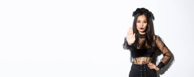 Kendine güvenen genç cadı dur işareti yapıyor, cadılar bayramı kostümü giymiş kadın bir elini bir şeyi yasaklamak için uzat, onaylamadığını ifade et, beyaz arka plan.