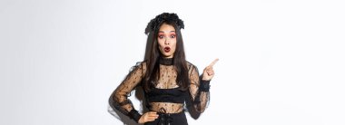 Cadı kılığındaki çekici Asyalı kadın sol üst köşeyi işaret ediyor, cadılar bayramı reklamı, parti tanıtımı yapıyor. Siyah gotik elbiseli güzel bir kadın. Şaşırmış görünüyor..
