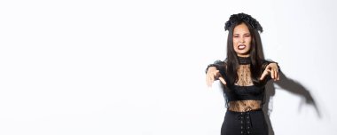 Cadılar bayramında birini lanetleyen güzel ölümsüz kötü cadının görüntüsü. Parti kostümlü kız ellerini ileri uzat ve korkutucu görün, şeker toplamaya git, beyaz arka planda dur..