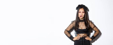 Sinirli ve rahatsız edici kötü cadı karışık görünüyor ve alt dudağı ısırıyor siyah dantelli elbise ve çelenk içinde beyaz arka planda duruyor. Cadılar bayramı kostümlü kız şaka mı şeker mi?.