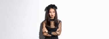 Gotik dantelli elbise ve çelenk giymiş deli Asyalı bir kadın tasviri. Kol göğsü çapraz, çatık kaşlı ve somurtkan. Sol üst köşede, beyaz arka planda dikiliyor..