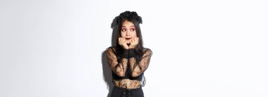 Gotik dantel elbiseli aptal Asyalı kız solda rüya gibi görünen çelenk, nostaljik düşüncelere sahip, cadılar bayramı kostümünün içinde beyaz arka planda duruyor..