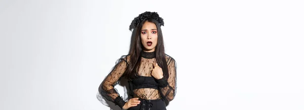 白い背景の上に立って パーティーに邪悪な魔女の黒いドレスを着て 自分自身を指してハロウィンの衣装で侮辱と混乱アジアの女性 — ストック写真