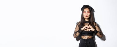 Güzel Asyalı gotik kız gözlerinizi kapatın ve öpücük için somurtun, kalp hareketi gösterin, Cadılar Bayramı partisinde sevgi ya da sempati gösterin, beyaz arka planda durun..