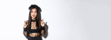 Gotik dantelli elbisesi ve siyah çelengi olan umut dolu Asyalı kadın, sol üst köşeye bakıyor ve şans diliyor, dilek diliyor ya da dua ediyor, beyaz arka planda duruyor..