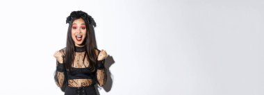 Cadılar bayramı partisi elbisesi içinde mutlu Asyalı gotik kız imajı, zafere sevinen, zafer kazanan ve evet diyen, zaferi kutlayan beyaz arka planda duran.