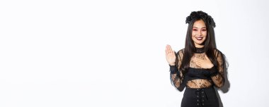 Cadılar bayramı kostümü giymiş, söz veren, yemin ederken, dürüst davranan, beyaz arka planda duran sevimli, samimi Asyalı bir kız resmi..