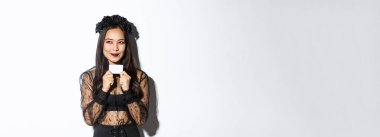 Siyahi gotik elbiseli düşünceli Asyalı kadının bir planı var, kredi kartı tutuyor, sol üst köşeden gülümsüyor..