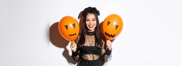 ハロウィンを祝う魔女の衣装で陽気なアジアの女性のイメージ 怖い顔と風船を保持 白い背景の上に立って — ストック写真