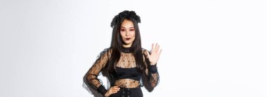 Cadılar Bayramı kostümü giymiş kendine güvenen güzel Asyalı kadın beş parmağını gösteriyor, merhaba demek için elini kaldırıyor, beyaz arka planda duruyor..