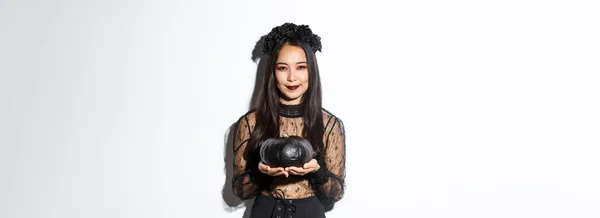 アジアの女の子を笑顔で魔女の衣装で ハロウィンを祝い 黒カボチャを保持し 白い背景の上に立って — ストック写真
