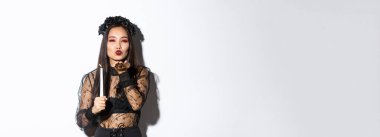 Güzel ve zarif Asyalı kadın gotik dantelli elbiseler içinde cadılar bayramını kutluyor, cadı gibi giyiniyor, kameraya hava öpücüğü gönderiyor ve elinde mum tutuyor..