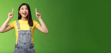 Kaygısız, eğlenceli Asyalı esmer, sarı tişörtlü, şaşkın ve büyülenmiş bir şekilde gülümseyen, yukarı bak, yeni bir tanıtım izle, heyecanla gülümse, üst fotokopi alanının keyfini çıkar..