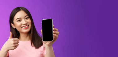 Yakın plan mutlu, çekici, çağdaş Asyalı kadın olumlu geri bildirim veriyor, akıllı telefon ekranını gösteriyor, iyi uygulama tanıtıyor, uygulama gibi başparmağını kaldırıyor, mor arka planda mutlu duruyor..