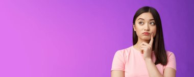 Çok düşünceli, tatlı Asyalı kız. Mor arkaplan, yanağa dokun, sola dön, düşün, nasıl davrandığını düşün, bilgiyi merak et, pencereden manzarayı seyret..