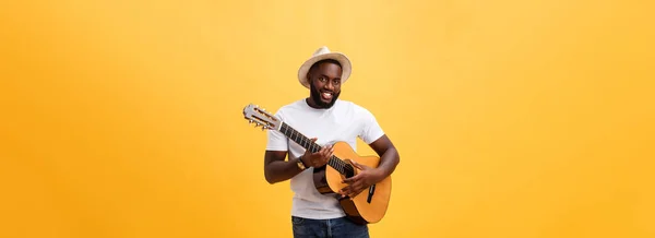 Muscular black man playing guitar, wearing jeans and white tank-top. Isolate over yellow background