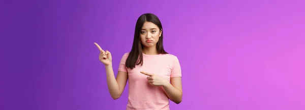 残念なことにかわいいアジアの女の子が競争を失い 不幸な笑みを浮かべて 右を指して 後悔と悲しみで横に指を示す 自分自身の同情を感じる 立って紫色の背景 — ストック写真
