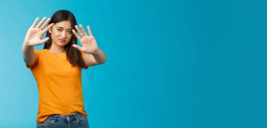 Asyalı huysuz aptal ürkek kız ışığın sönmesini, fotoğrafının çekilmesini istemiyor, ellerini kaldırıyor, yüzünü kapatıyor ve hayal kırıklığına uğruyor, mavi arka planda durmaktan çekiniyor. Boşluğu kopyala