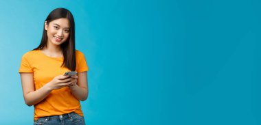 Neşeli, arkadaş canlısı, Asyalı kız öğrenci mesajlaşması arkadaşı, akıllı telefon mesajlaşması takipçileri, yeni internet uygulaması kullanarak, uygulama standı deneyin gülümseyen kamera, mavi arka plan.