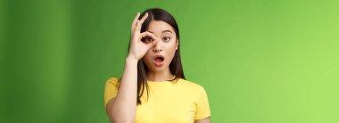 Şaşırtıcı dilsiz, tatlı Asyalı genç kız, çeneni indir, şaşırt, çember işaretine bak, çeneni indir, nutkun tutulsun, etkileyici kamera, inanılmaz tanıtıma bak, yeşil arka planda dur.