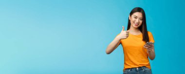 Tatmin olmuş tatlı Asyalı esmer kız. Akıllı telefon göster. Başparmağını kaldır, harika bir cihaz tavsiye et, yeni bir uygulama onayla..