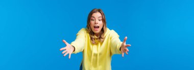 Bir şey yakalamaya çalışan, çocuklarla oynarken odaklanmış ve eğleniyor gibi görünen, ellerini uzatan ve konsantre ifade ile nesneleri okumak için öne doğru eğilen, mavi arka planda duran bir kız..