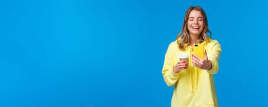 Neşeli gülümseyen sarışın beyaz kadın blogger video kaydı ya da akıllı telefonuyla selfie çekip, kahkahalar atarak kahkahalar atarak kahkahalar atarak, mavi arka planda durmak..