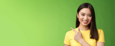 Neşeli, yakışıklı Asyalı esmer, mükemmel tanıtım fırsatı sunuyor, işaret parmağını sola gösteriyor, gülümseyerek mutlu bir şekilde ürünü tanıtmaya yardım ediyor, yeşil arka planda duruyor. Boşluğu kopyala