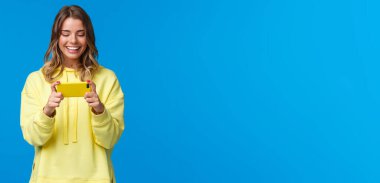 Yemek molasında dinlenme zamanı. Kaygısız, yakışıklı, sarı kapüşonlu hippi kız oynamak için cep telefonunu kullanıyor, akıllı telefonu yatay pozisyonda tutuyor ve kolay bir oyun olarak gülümsüyor..