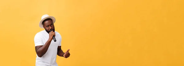 感情的なモーション ジェスチャーで 黄色の背景に分離されたマイクを使って歌っているハンサムなアフリカ系アメリカ人少年 — ストック写真
