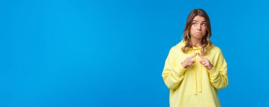 Utangaç ve aptal kawaii sarı kapüşonlu sarışın utangaç kız seni sevdiğimi söyle, parmaklarını sok ve göz teması kurmamak için yüzünü çevir, soracak bir şeyin olsun, mavi arka plan.