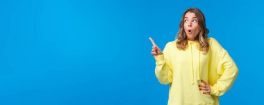 Heyecanlı, dilsiz, sarı kapüşonlu sarışın kadın şok edici ve ilginç bir şeye tepki veriyor. Parmakla işaret edip sola bakıyor ve 