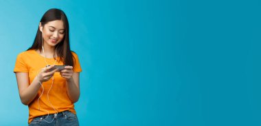 Mutlu Asyalı tatlı kız esmer, kulaklık takıyor kafede en sevdiği akıllı telefon oyununu oynarken rahatsız etmiyor, telefonu yatay tutuyor, gülümsüyor cep telefonu ekranına bakıyor..
