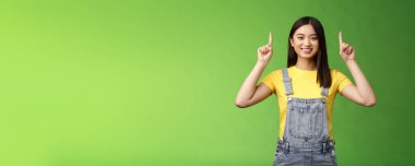 Dost canlısı, yakışıklı Asyalı esmer kadın işaret ediyor, parmaklarını en üstteki reklama kaldırıyor, kendine güvenen tanıtım yapıyor, gülümsüyor, tatmin oluyor, yeni ürün tanıtıyor, yeşil arka plan.