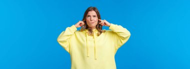Disturbed and bothered young blong woman with pissed-off expression, grimacing boiling from annoyance and anger at her loud neighbours, shut ears cursing in mind look up.