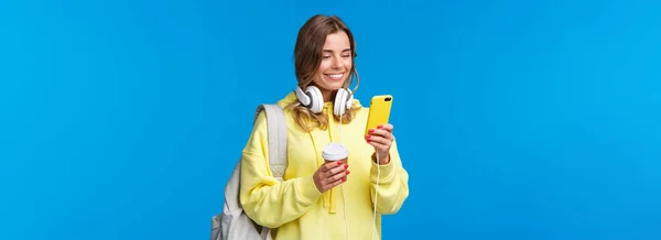 女大学生大学毕业后用手机与朋友联系 带着背包 咖啡杯和耳机在街上走来走去 开心地笑着展示智能手机 — 图库照片