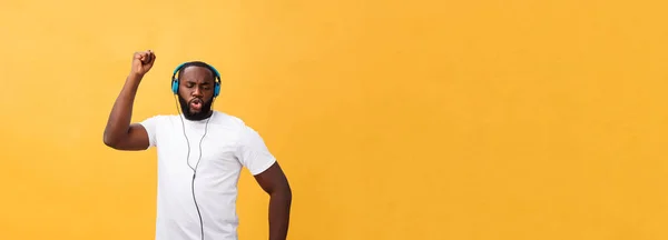 若いアフリカ系アメリカ人の男は身に着けているヘッドフォンとイエローゴールドの上に踊る音楽を楽しむ背景 — ストック写真