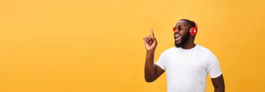 Dinleme ve müzik üstünde hareket eden aygıt ile gülümseyen yakışıklı genç Afro-Amerikan adam. Sarı arka plan üzerinde izole