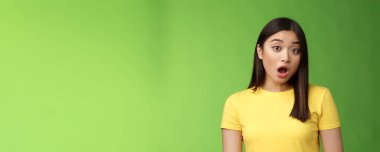 Yakın çekim şoke olmuş Asyalı esmer kadın şaşkına dönmüş, nefes kesici dedikodular duyuyor, suskun kamera konuşamıyor, sersemlemiş yeşil arka plan, ne olduğuna şaşırmış, sarı tişört giyiyor..