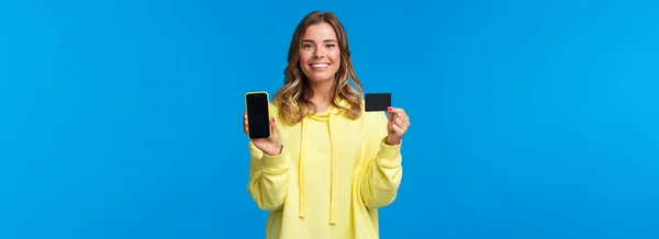 银行和金融概念 使用信用卡 展示和智能手机显示快乐微笑的金发女孩的肖像 对新的应用感到满意 有助于网上购物 蓝色背景 — 图库照片
