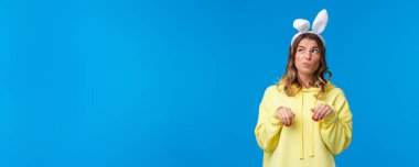 Düşünceli ve sevimli komik sarışın kız. Sahte kulaklı ve pençeli Paskalya tavşanı gibi davranıyor. Sol üst köşeye bakıp tavşan taklidi yapıyor..