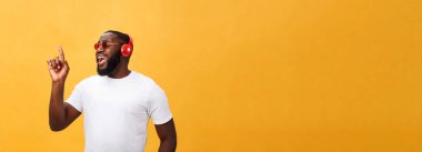 Dinleme ve müzik üstünde hareket eden aygıt ile gülümseyen yakışıklı genç Afro-Amerikan adam. Sarı arka plan üzerinde izole