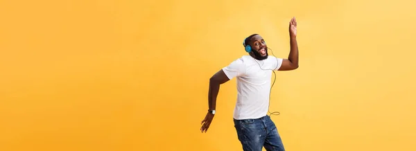 一个樱桃年轻的非洲裔美国男子的全长肖像听音乐与耳机和舞蹈孤立的黄色背景 — 图库照片